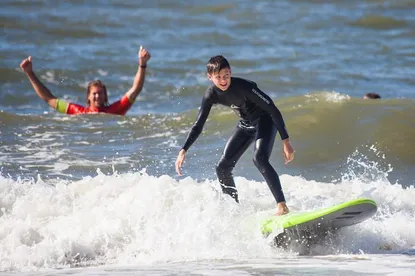 Surfleraar juicht in het water terwijl surfer surft